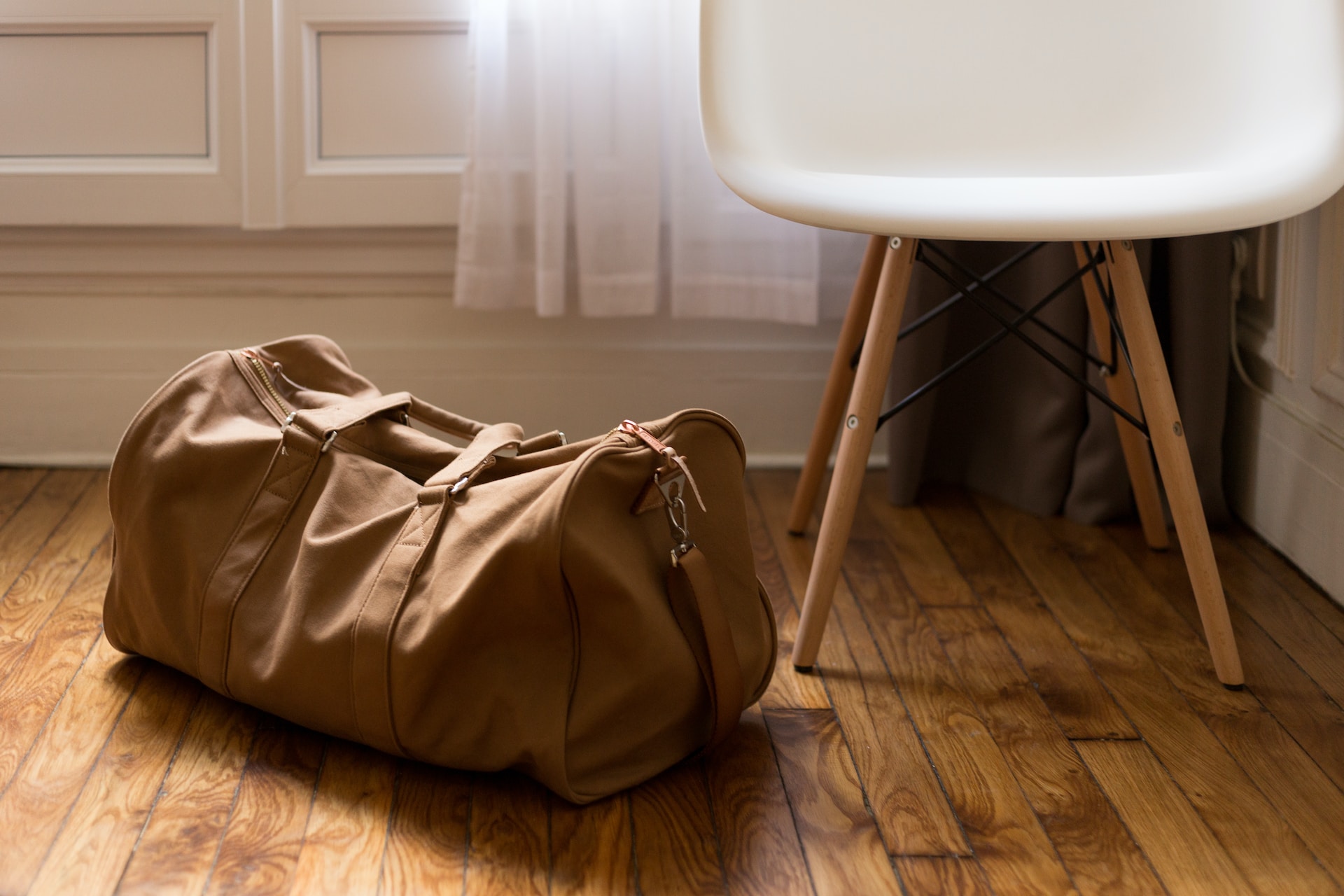 A beige duffle bag sits packed next to a chair