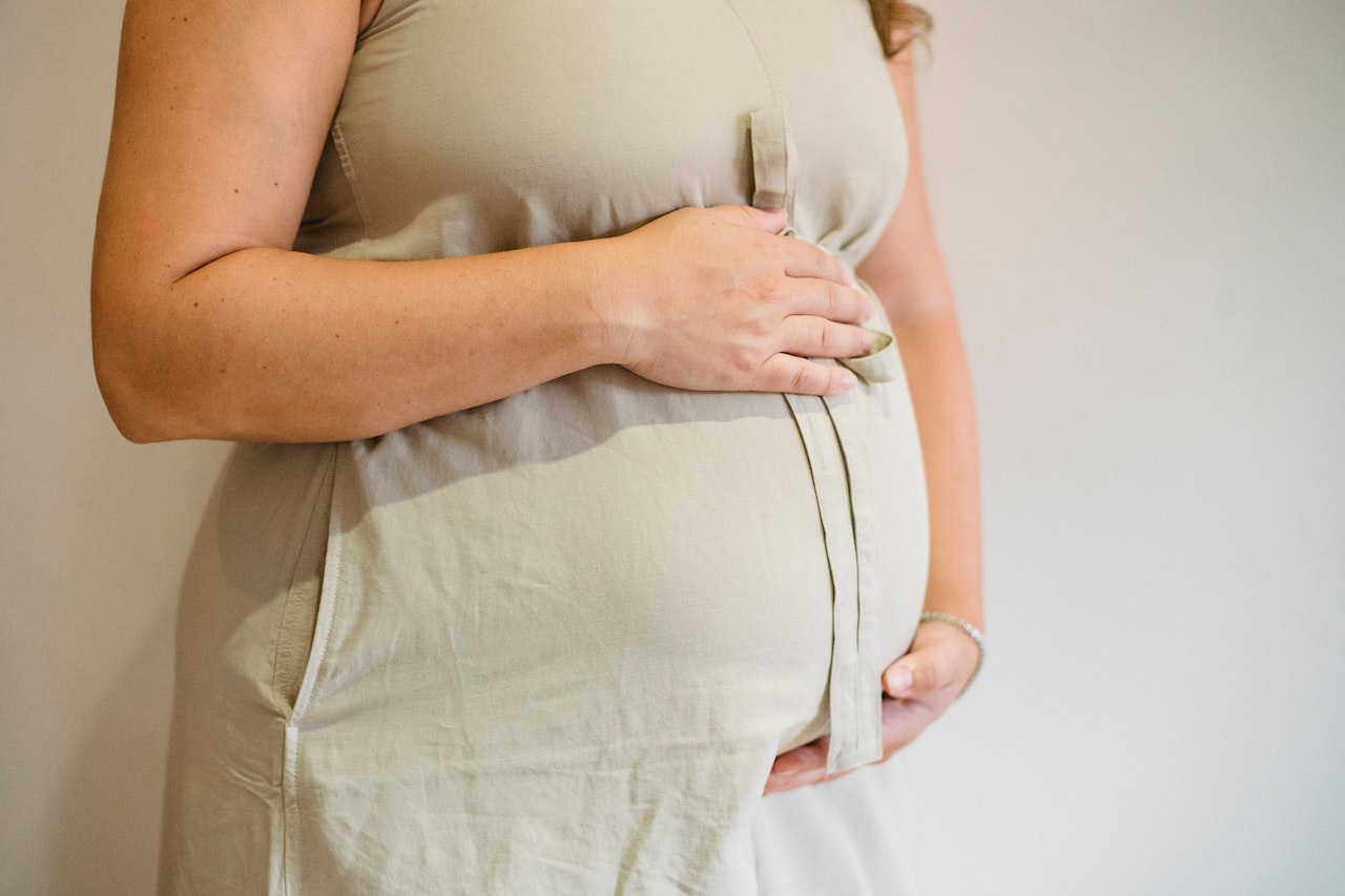 Woman wearing a beige dress holding her pregnant belly