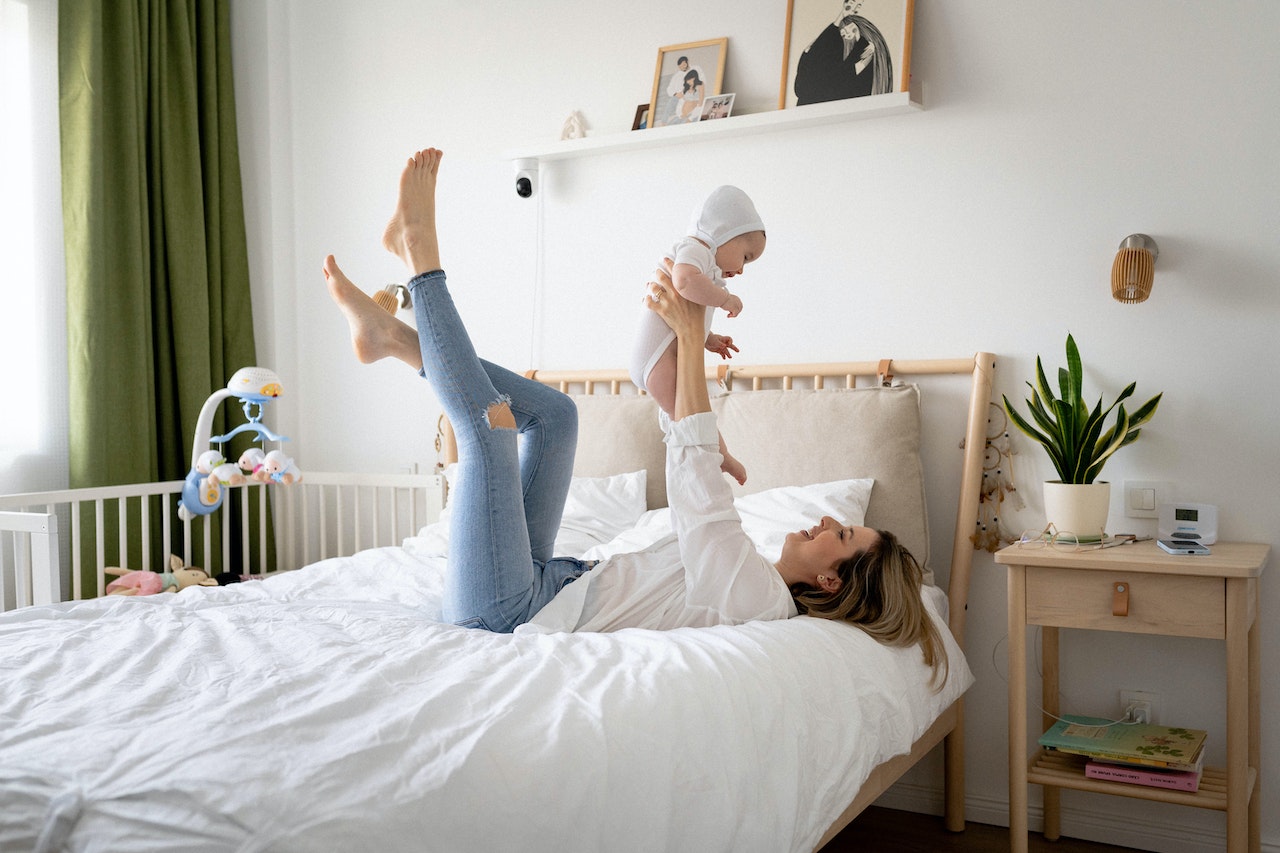 New mom lying in bed holding her baby up above her head and smiling